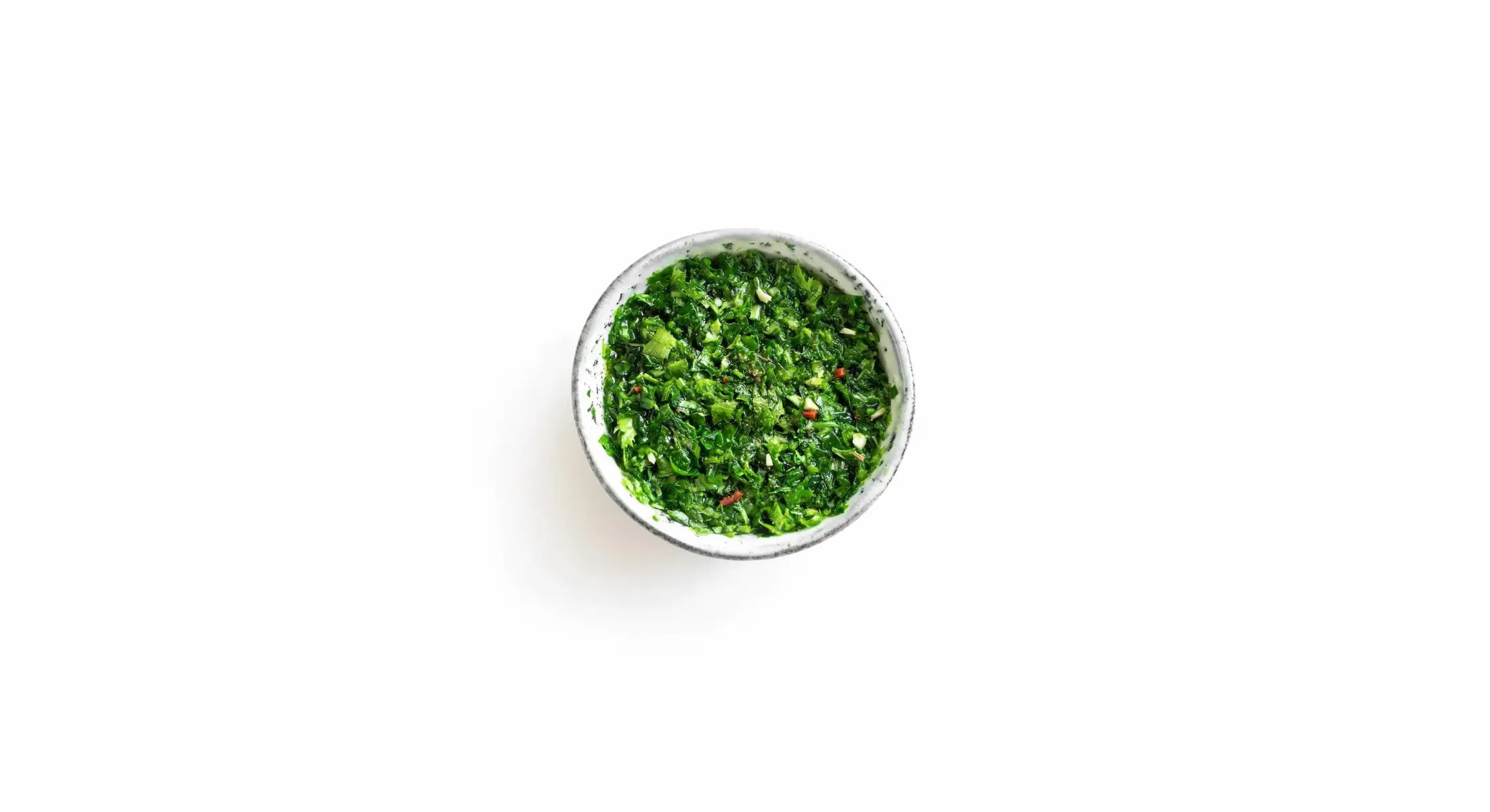 Small bowl of vibrant green chimichurri sauce with chopped herbs and spices