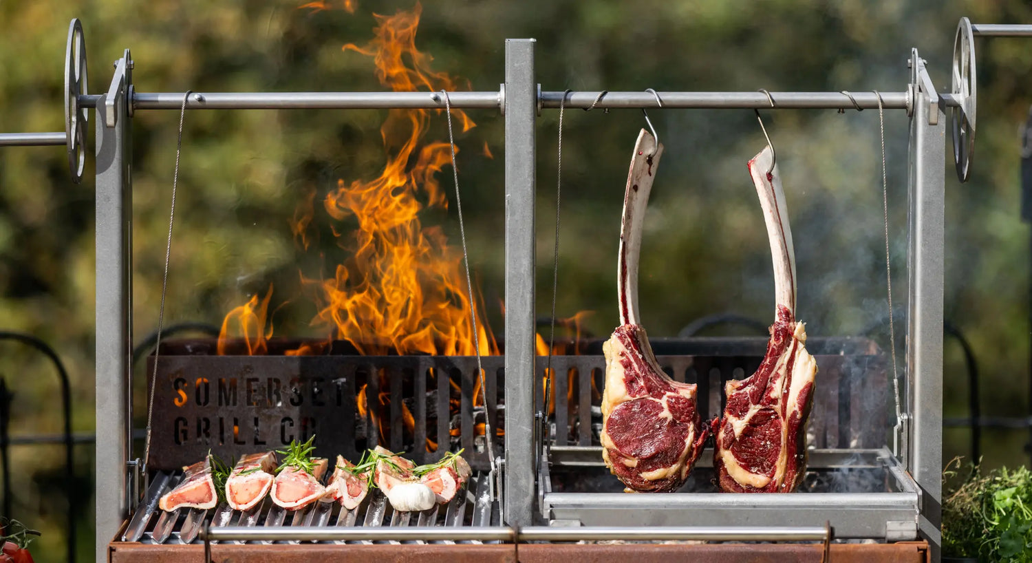 Stainless steel custom grill with hanging tomahawk steaks and lamb chops over open flame