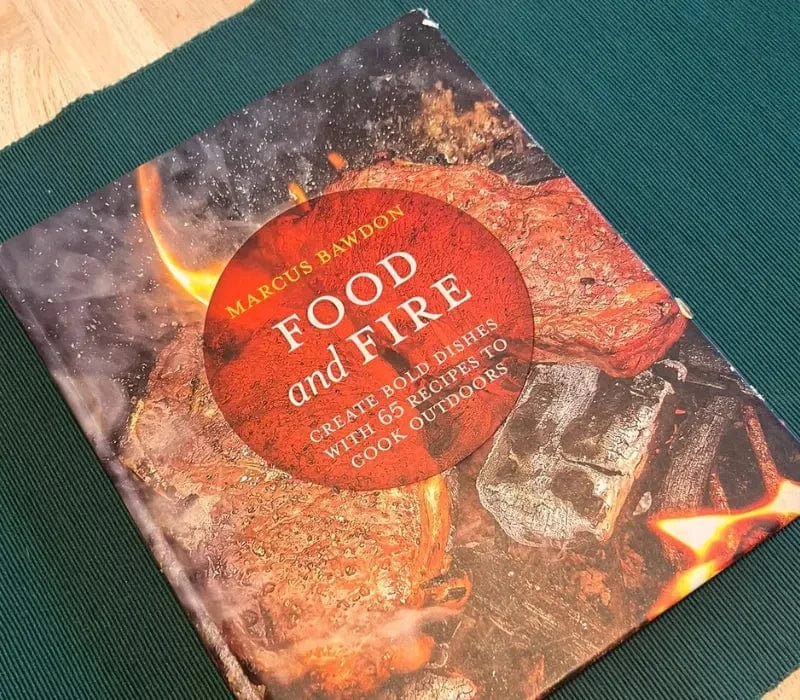 Cookbook titled Food and Fire by Marcus Bawdon with grilled meat and flames on cover