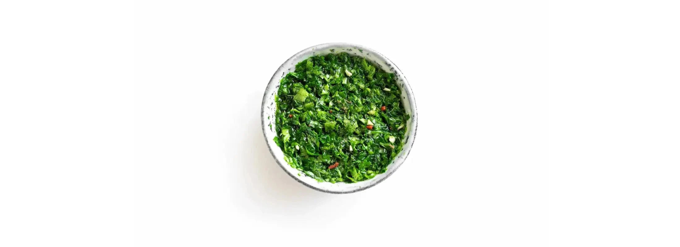 White bowl filled with finely chopped green chimichurri sauce with herbs and spices