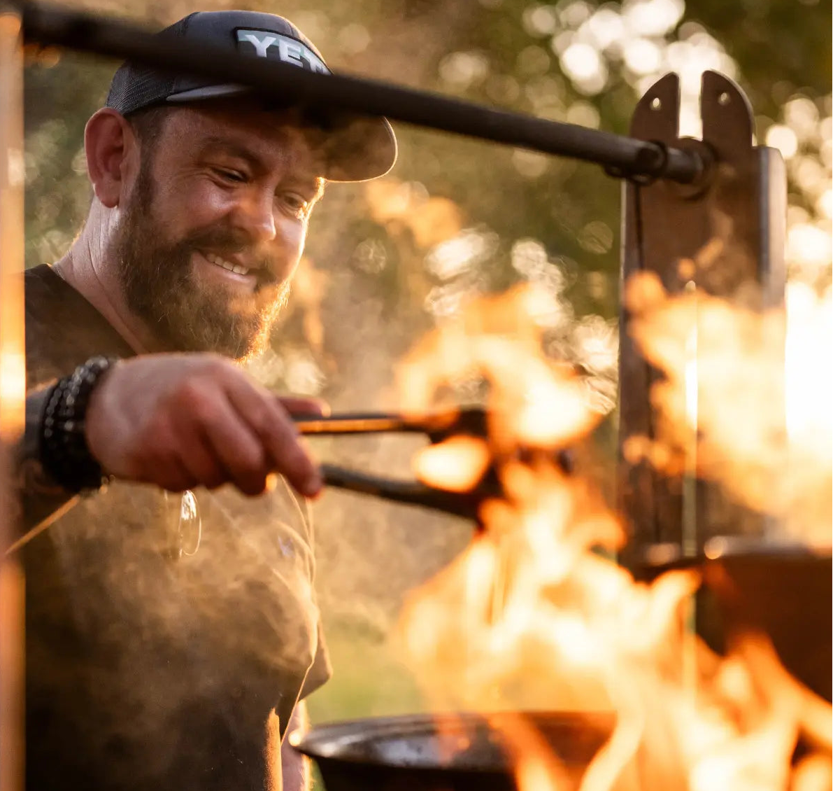 Man roasting food over an open fire with a hat on
