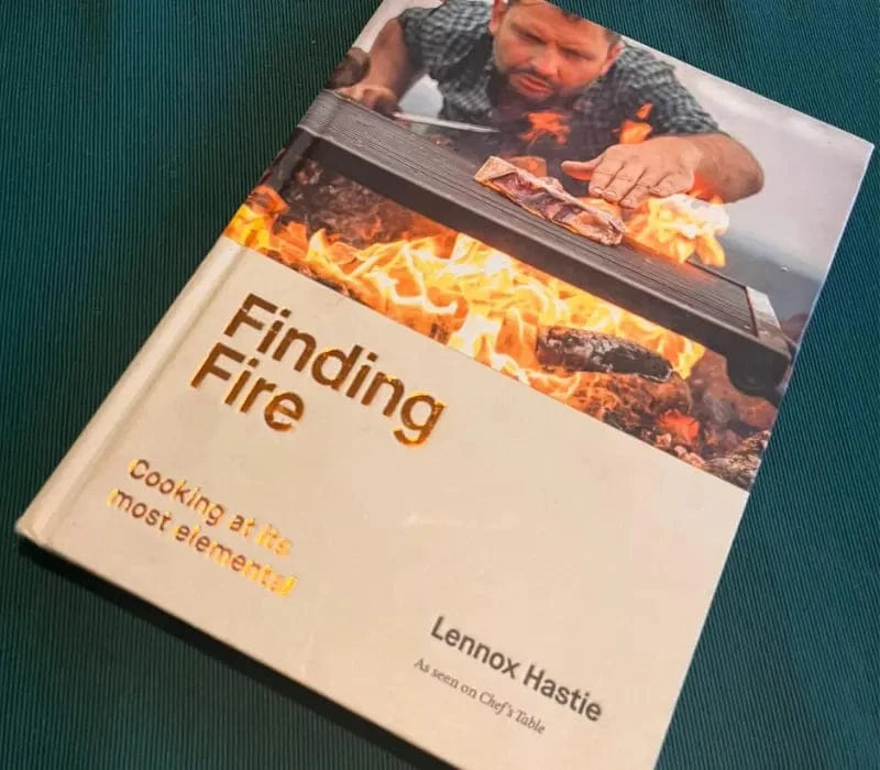 Cookbook titled Finding Fire by Lennox Hastie with cover photo of man cooking over open flames