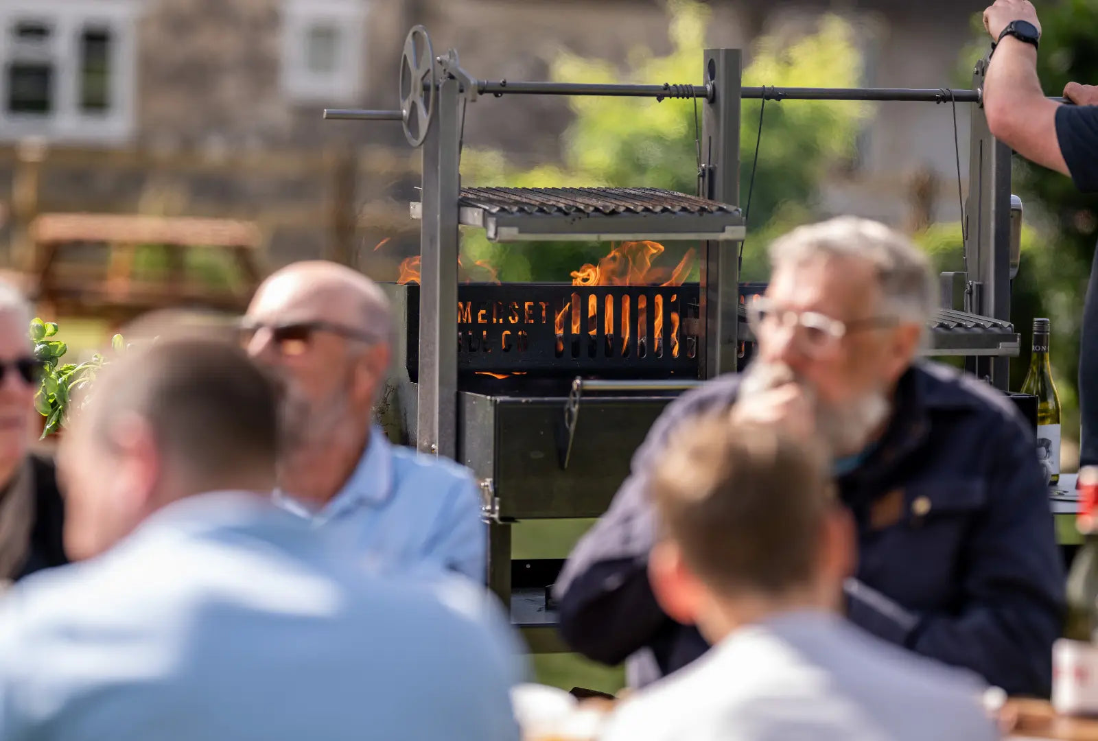 Gunmetal grey outdoor kitchen bundle with adjustable grill and fire pit, people socialising nearby