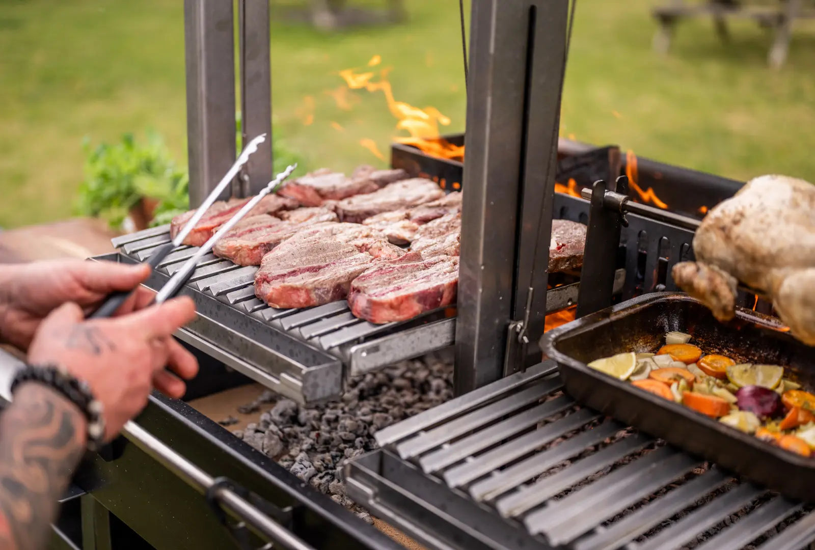 Gunmetal outdoor kitchen bundle with steaks grilling, rotisserie chicken, and vegetables roasting
