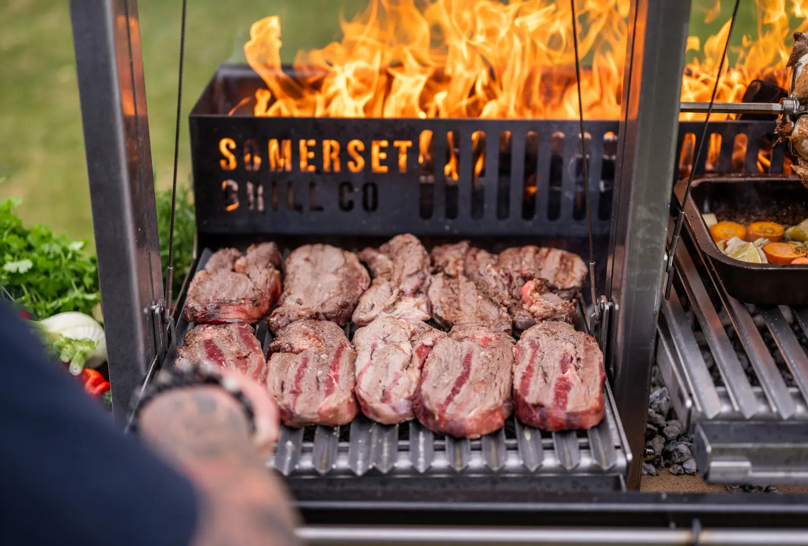 Gunmetal outdoor kitchen grill with multiple steaks cooking over an open flame