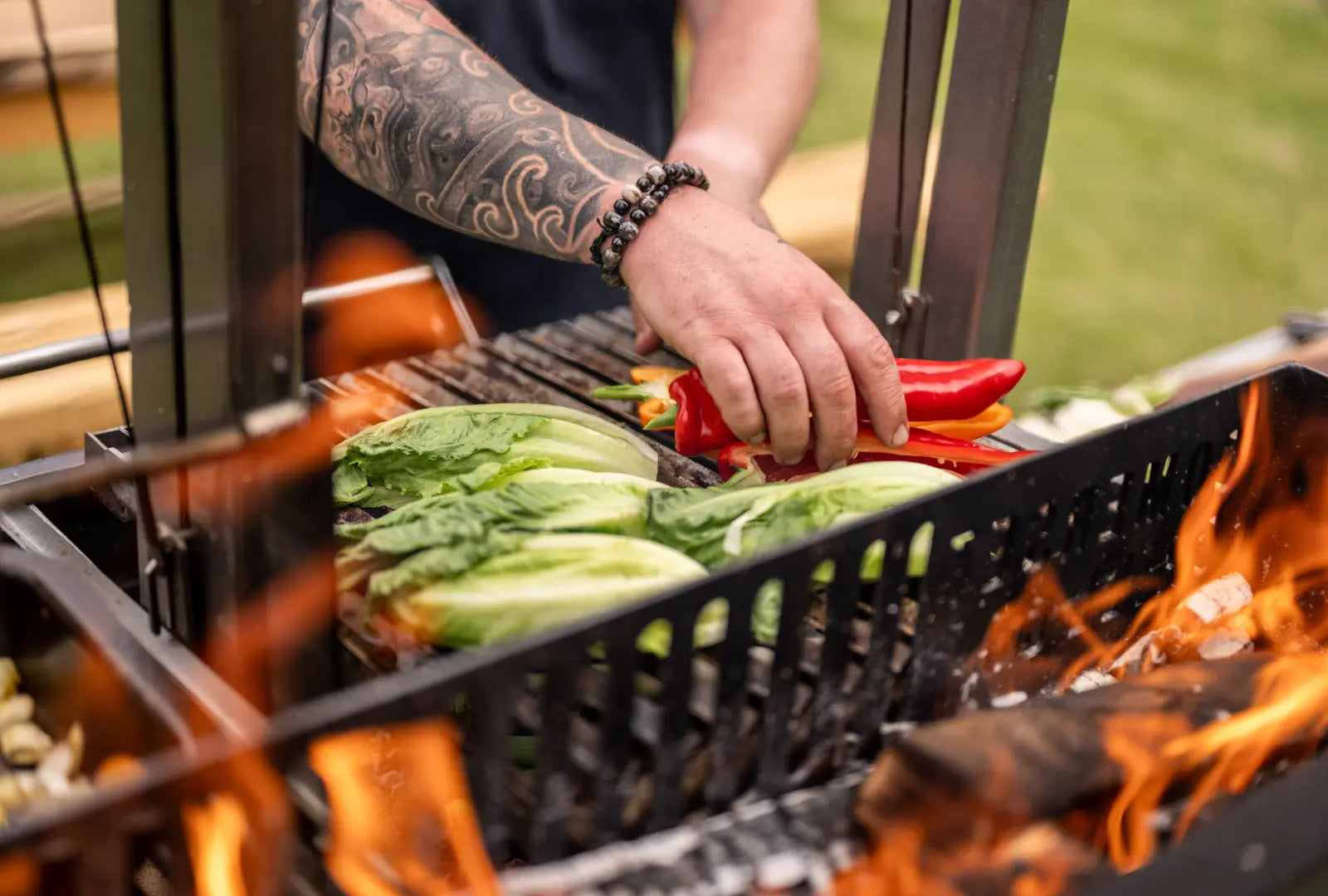 Gunmetal outdoor kitchen grill with fresh lettuce and red peppers being placed on the grate over open flames