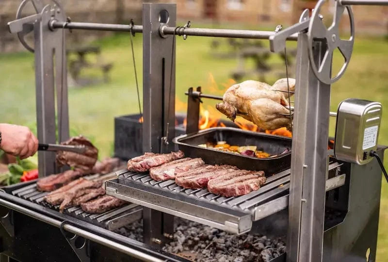 Gunmetal grey outdoor kitchen bundle with rotisserie chicken, steaks, and vegetables cooking over open flame