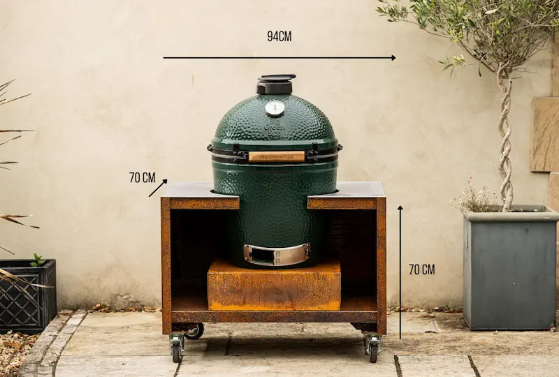 Large green ceramic Big Green Egg barbecue on rust-coloured Cor-Ten steel unit with wheels, outdoor setting