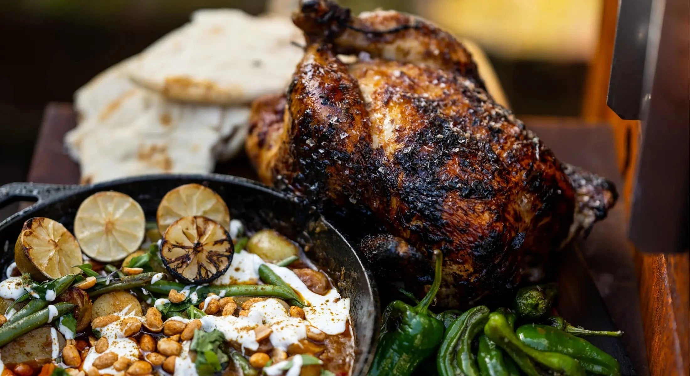 Charred whole roast chicken with grilled green peppers, flatbread, and curry with lime slices and peanuts