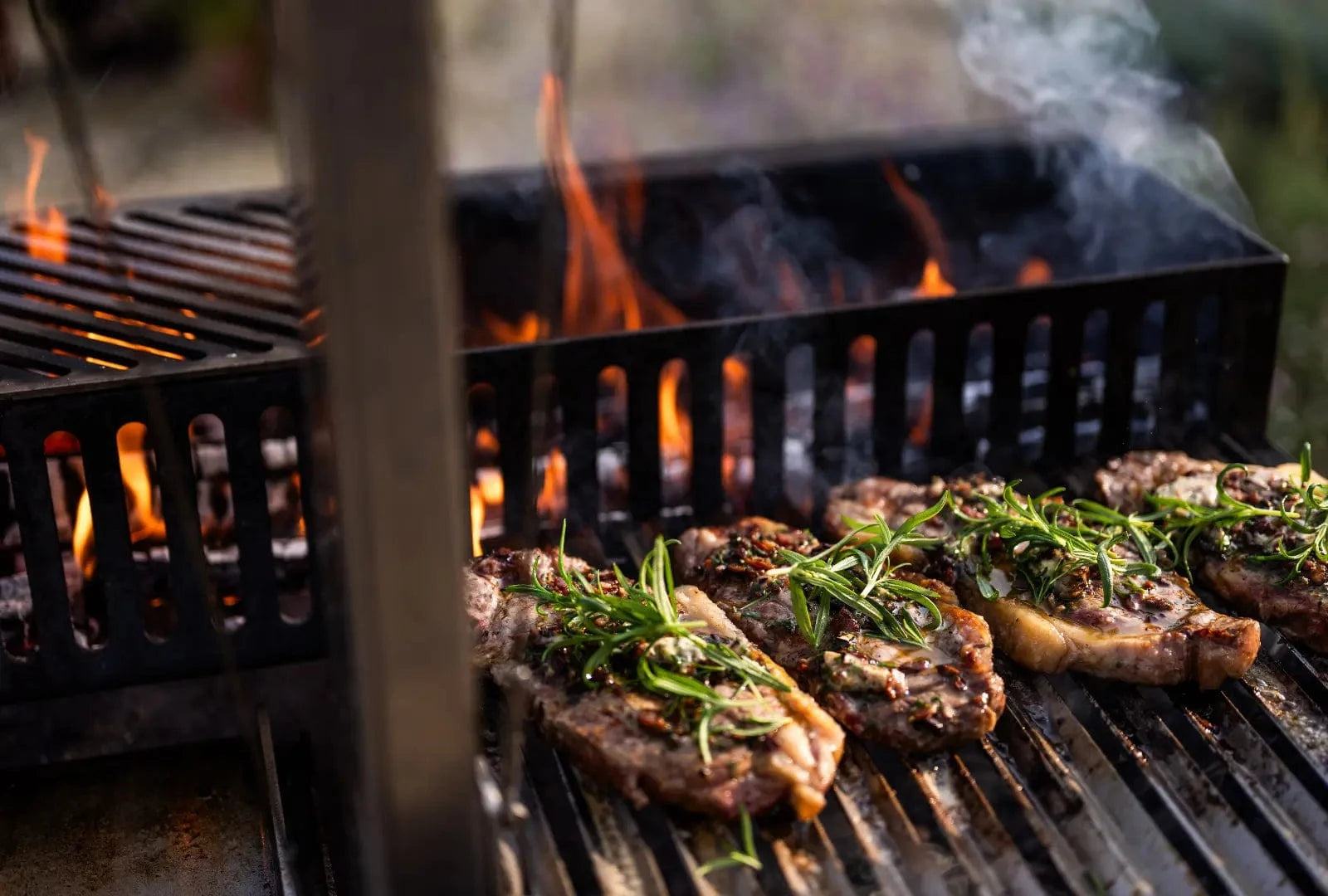 Gunmetal outdoor kitchen grill with steaks cooking, garnished with fresh rosemary and flames
