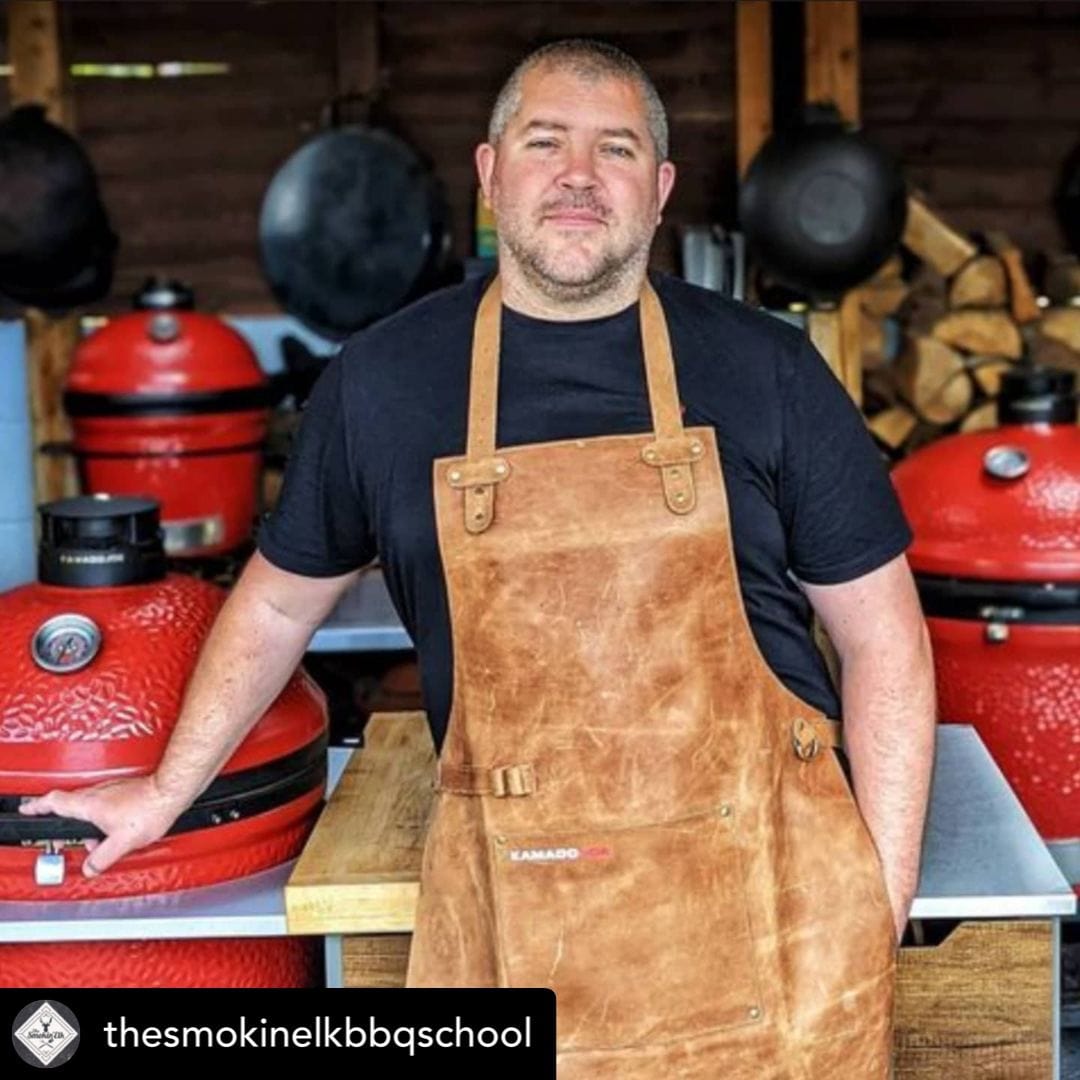 Brown leather apron worn by man standing in front of red ceramic barbecue grills