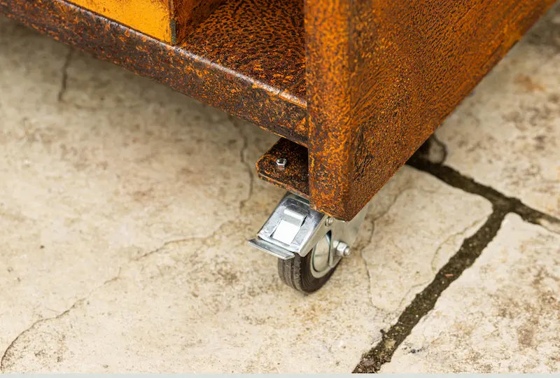 Close-up of rust-coloured Cor-Ten steel base with metal caster wheel on stone floor