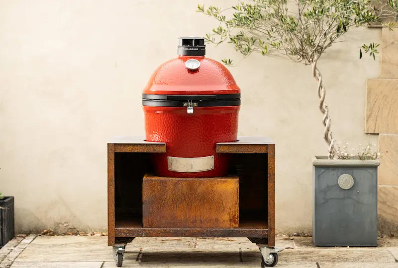 Red ceramic Kamado Joe grill on rust-coloured Cor-Ten steel stand with wheels outdoors