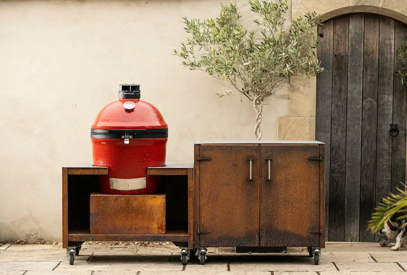 Classic Kamado Joe barbecue in red ceramic with Cor-Ten steel storage unit on wheels outdoors