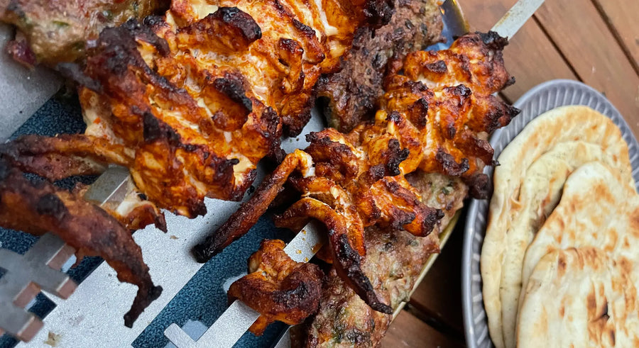 Grilled lamb seekh and chicken shawarma kebabs on metal skewers with flatbreads on a plate