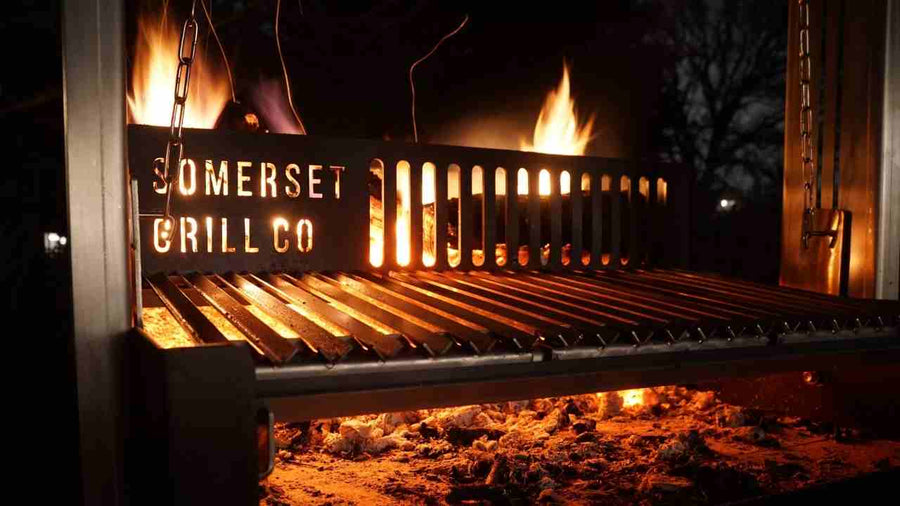 Black metal grill with flames and glowing embers, branded Somerset Grill Co, outdoor night setting