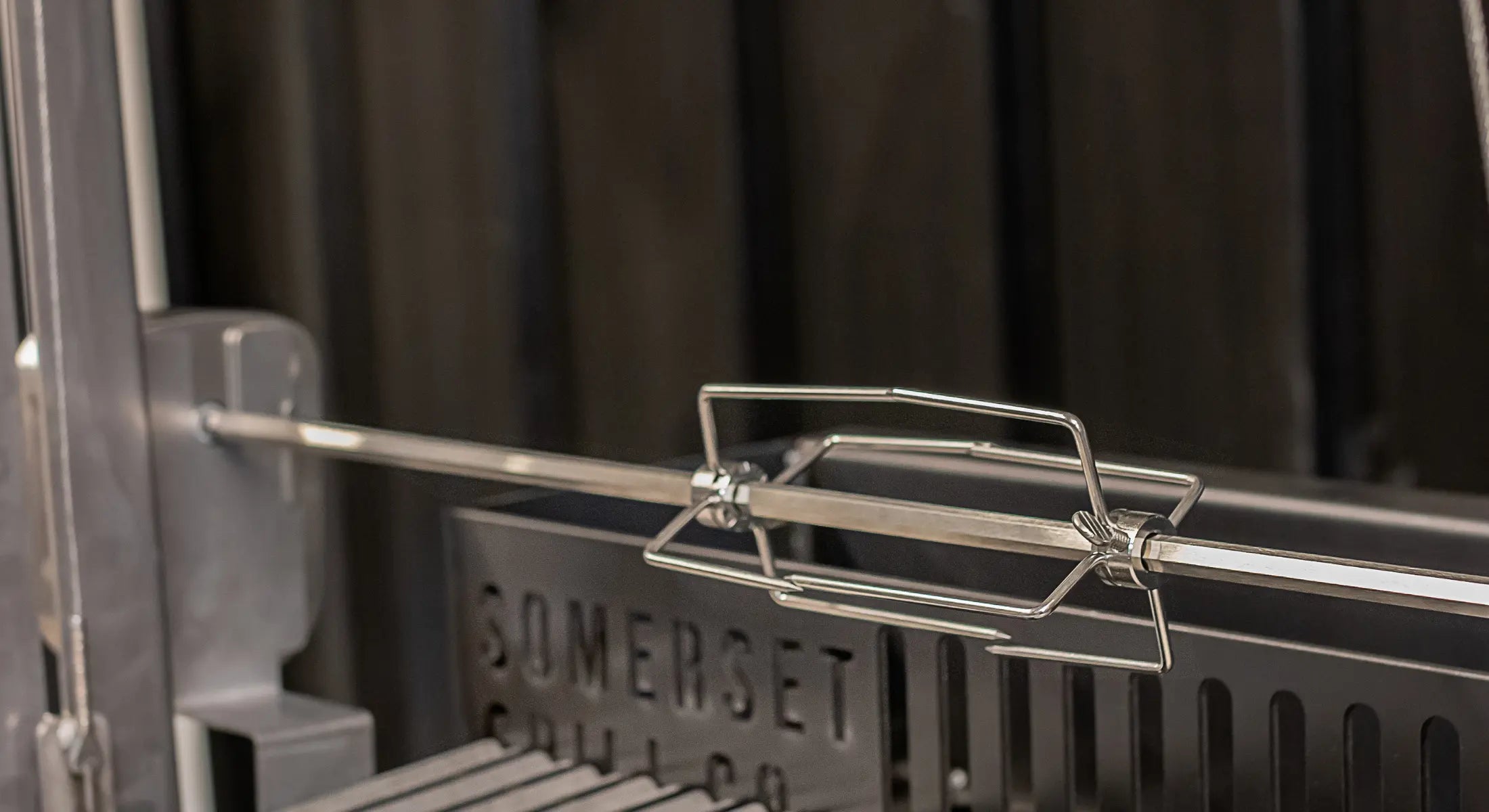 Stainless steel rotisserie spit rod with adjustable forks inside a barbecue grill
