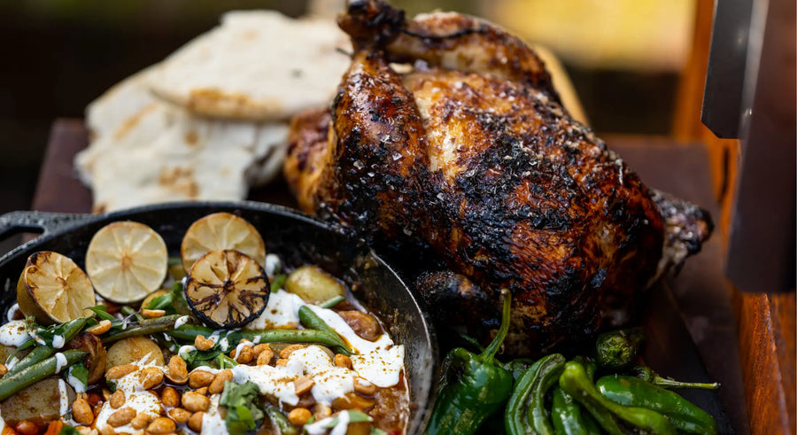 Chargrilled whole chicken with green peppers, flatbreads, and a skillet of curry garnished with lime and peanuts