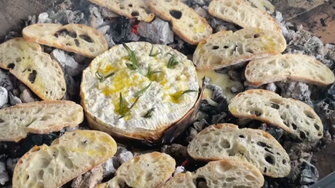 Round Camembert cheese baked on embers with rosemary and olive oil, surrounded by toasted sourdough slices