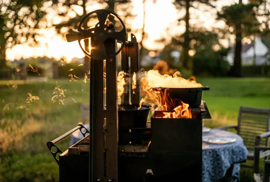 Black metal asado grill with flames and smoke, outdoor setting with table and chairs