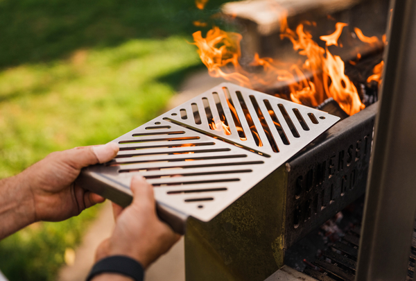 ember grill being put onto an asado stainless steel grill with flames in the background