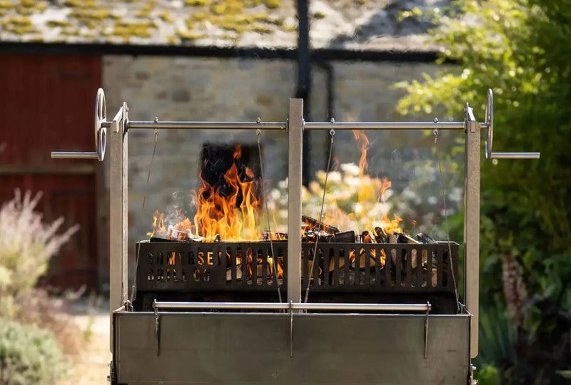 Gunmetal outdoor fire pit with adjustable spit roasting mechanism and burning wood