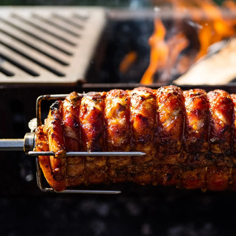 Golden-brown seasoned meat roasting on a metal rotisserie spit over open flames