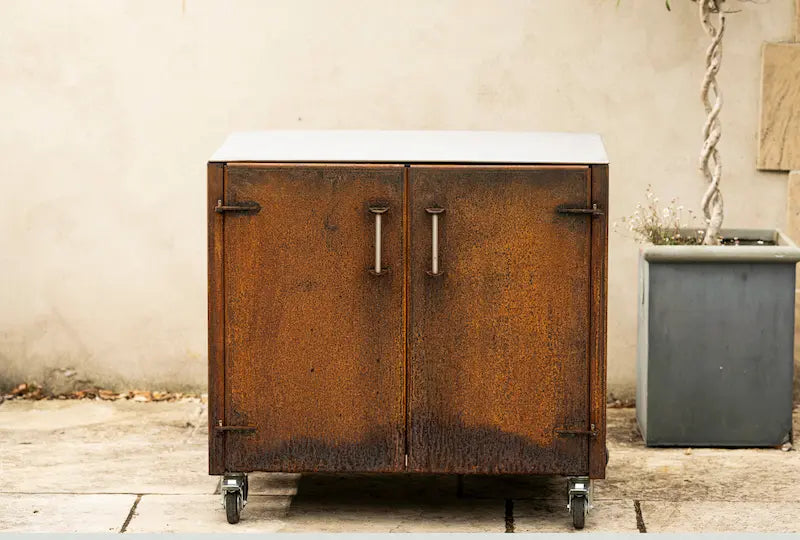 Rustic Cor-Ten steel worktop unit with double doors and metal handles on caster wheels