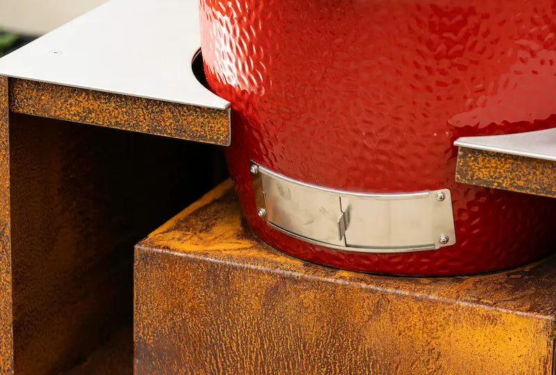 Close-up of Classic Kamado Joe barbecue with red ceramic body on rust-coloured Cor-Ten steel base